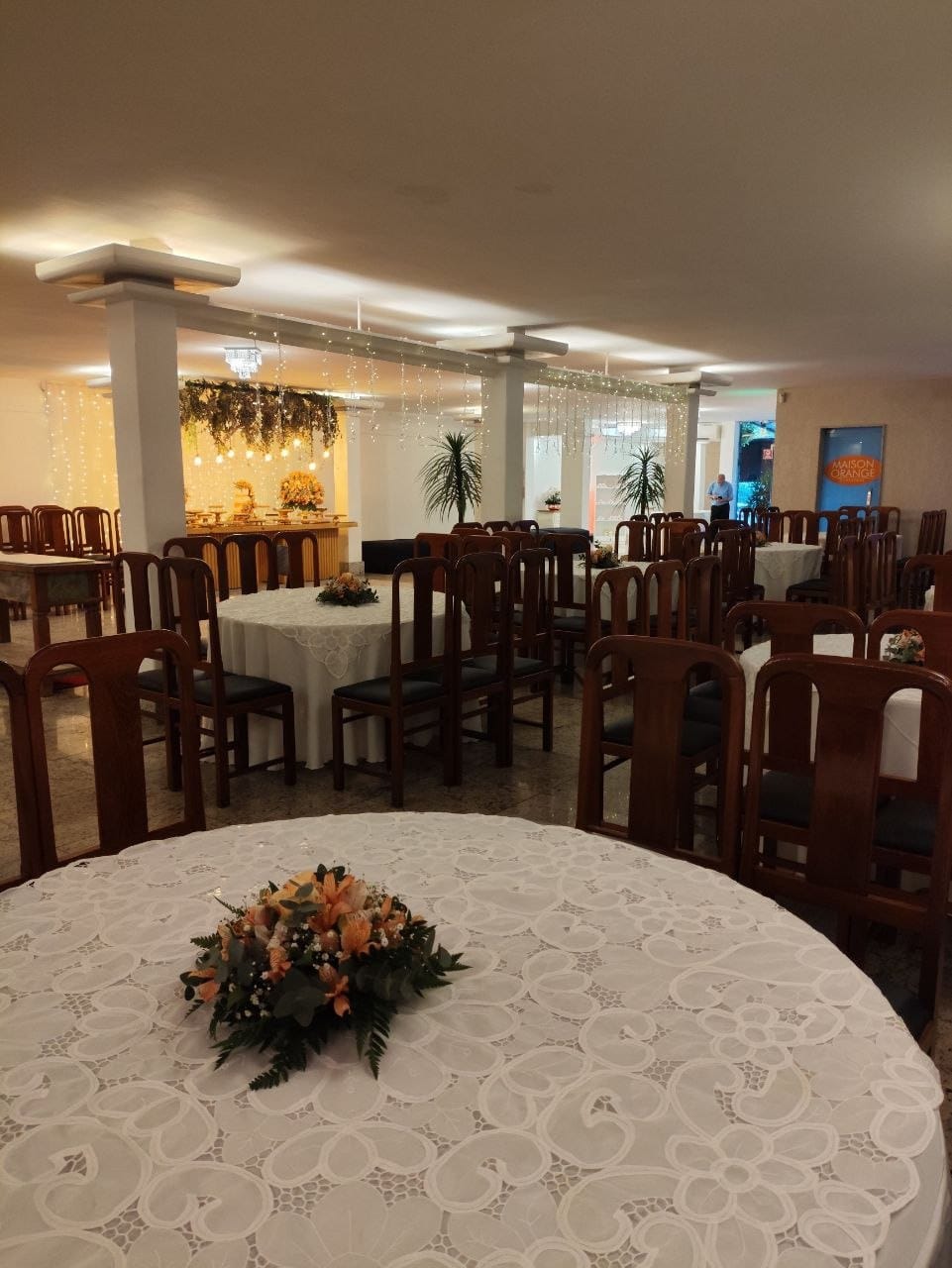 Salão da Maison Orange Classique com mesas redondas e arranjos em Vitória ES
